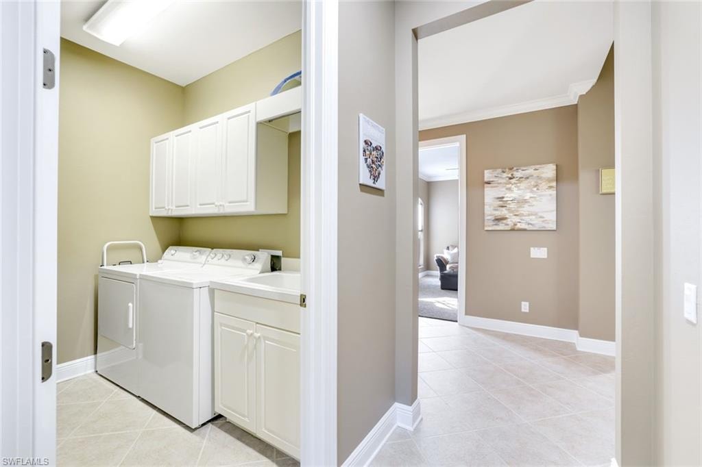 Laundry room featuring light tile patterned floors, cabinet space, washer and clothes dryer, and crown molding