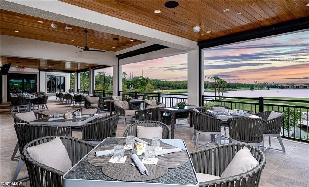 Patio terrace at dusk with outdoor dining space, ceiling fan, a patio area, an outdoor hangout area, and a water view