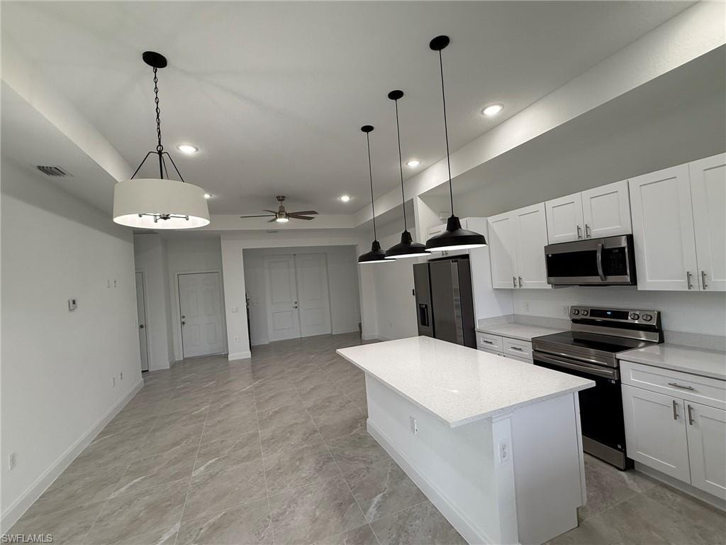 Kitchen with stainless steel appliances, white cabinets, a center island, hanging light fixtures, and recessed lighting