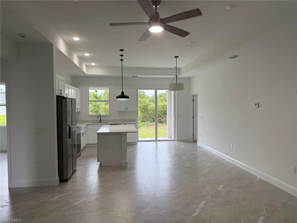 Kitchen with light countertops, white cabinets, stainless steel refrigerator with ice dispenser, a kitchen island, and pendant lighting