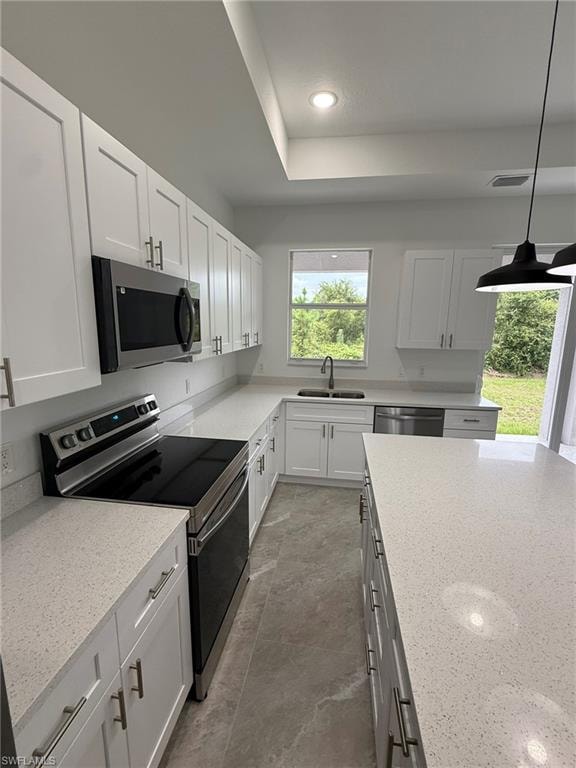 Kitchen with appliances with stainless steel finishes, white cabinets, light stone counters, pendant lighting, and recessed lighting