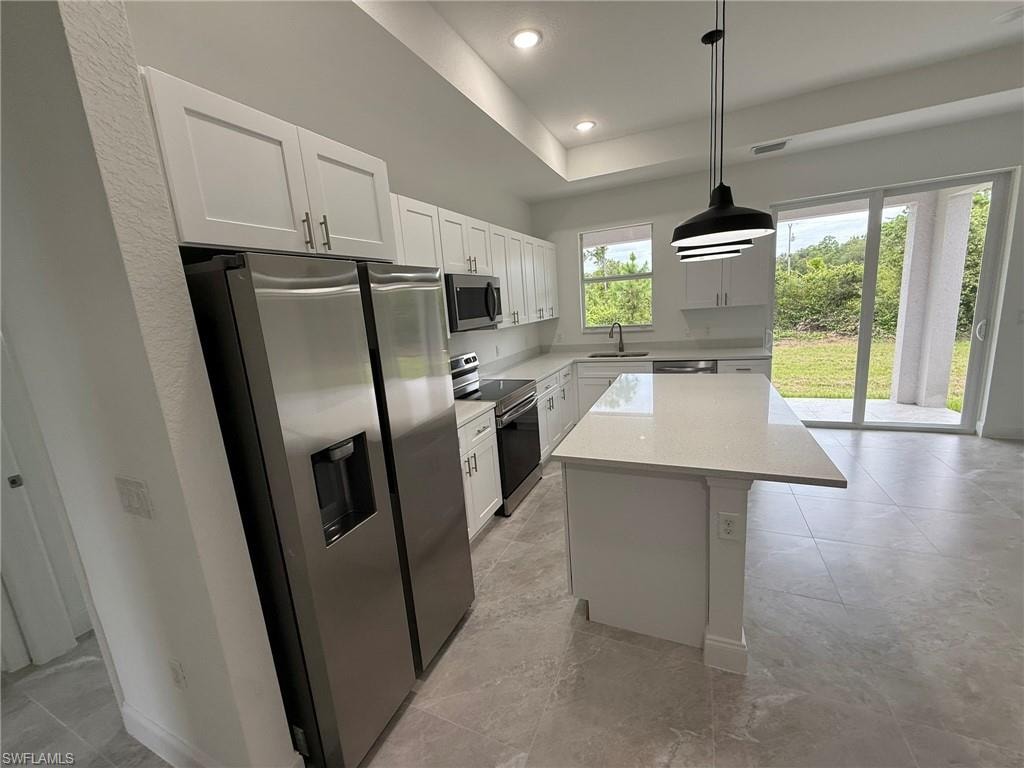 Kitchen with stainless steel appliances, a center island, white cabinets, a tray ceiling, and pendant lighting