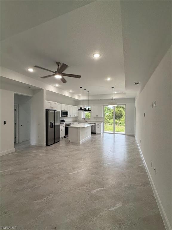 Kitchen featuring white cabinets, open floor plan, hanging light fixtures, appliances with stainless steel finishes, and a kitchen island