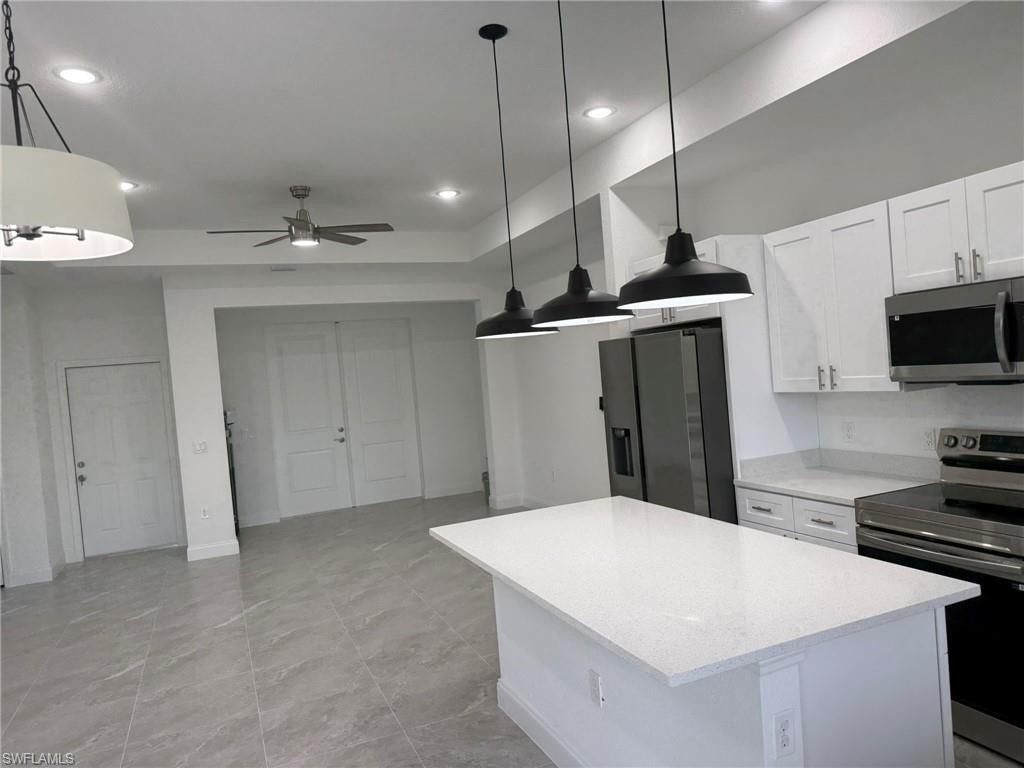 Kitchen with stainless steel appliances, white cabinets, hanging light fixtures, a kitchen island, and ceiling fan