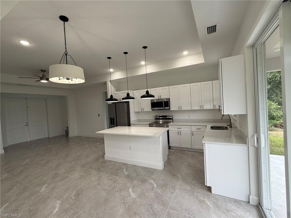 Kitchen with pendant lighting, a kitchen island, appliances with stainless steel finishes, white cabinetry, and light stone countertops
