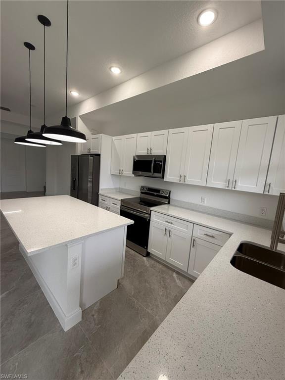 Kitchen with stainless steel appliances, white cabinets, light stone countertops, a center island, and recessed lighting