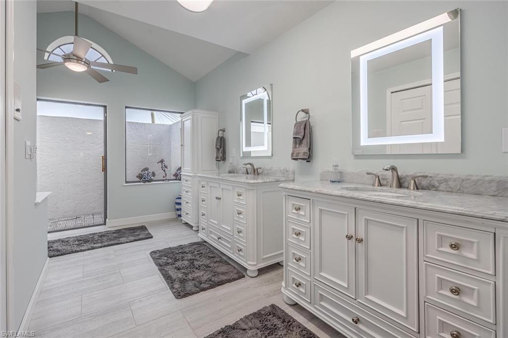 Bathroom featuring two vanities, vaulted ceiling, walk in shower, ceiling fan, and light wood-style flooring