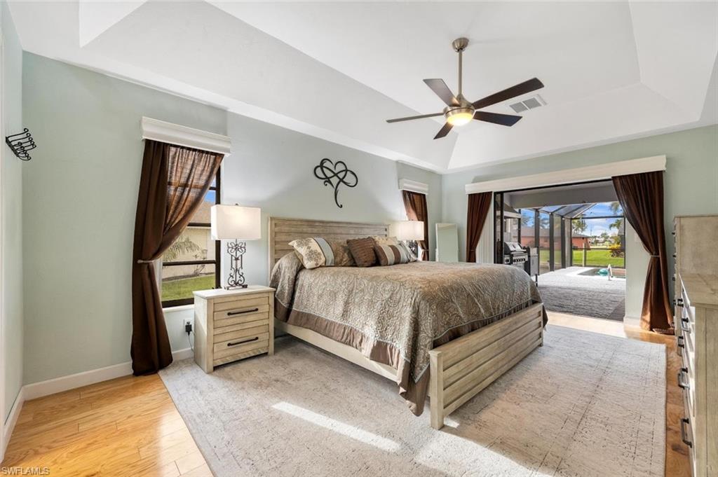 Bedroom with a raised ceiling, access to exterior, light wood finished floors, and a ceiling fan