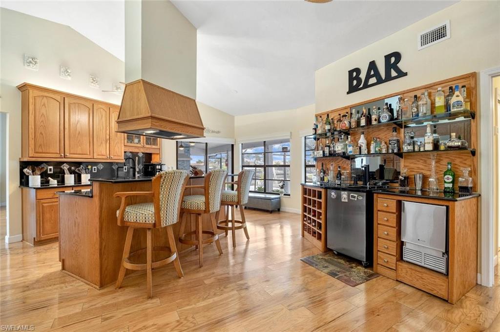 Kitchen with brown cabinetry, a breakfast bar, backsplash, open shelves, and dark stone counters