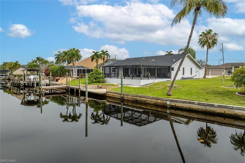 Back of property featuring a sunroom, boat lift, a lanai, a water view, and a lawn
