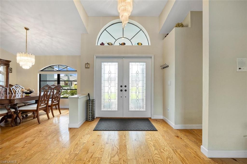 Entrance foyer with a chandelier, french doors, light wood-style floors, and a towering ceiling