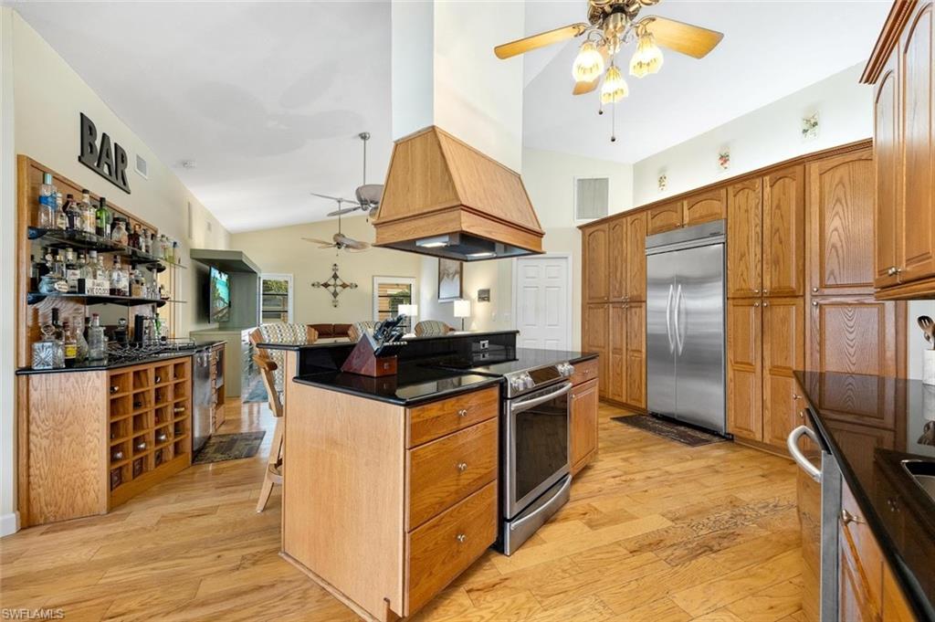 Kitchen featuring ceiling fan, stainless steel appliances, premium range hood, lofted ceiling, and light wood-style floors