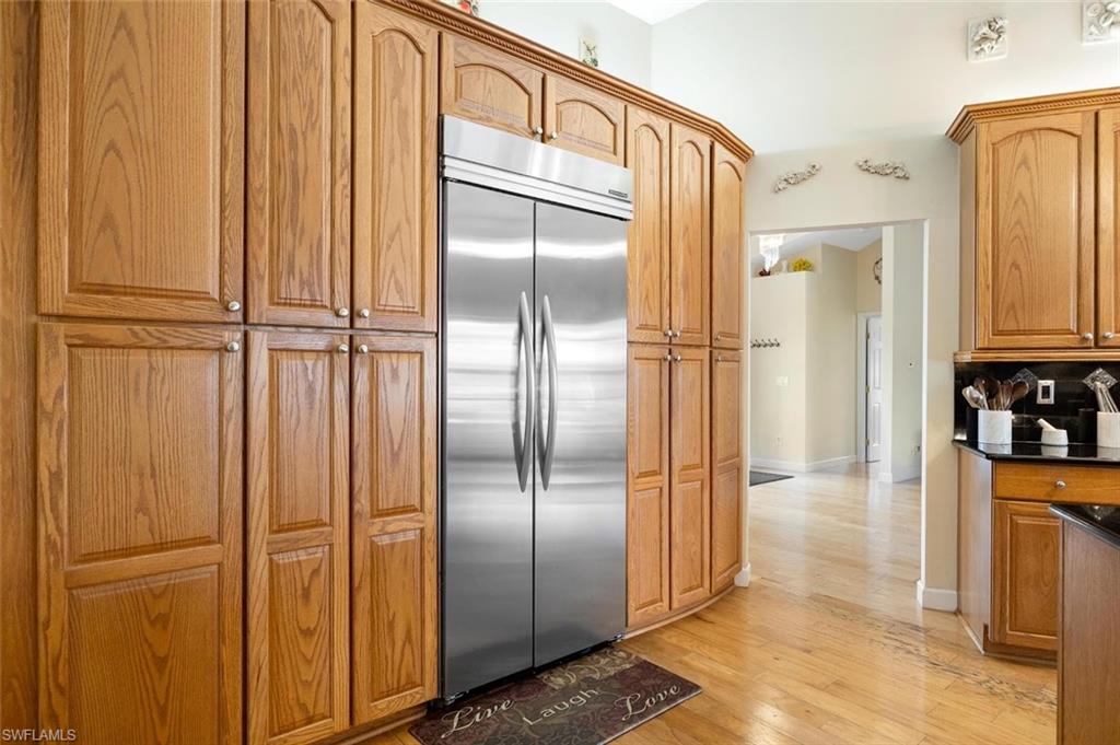 Kitchen featuring built in fridge, light wood-style flooring, brown cabinetry, and dark stone countertops