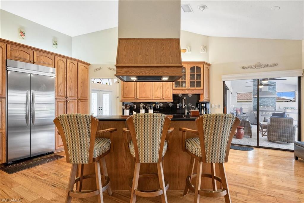 Kitchen with dark countertops, light wood-type flooring, built in fridge, brown cabinetry, and high vaulted ceiling
