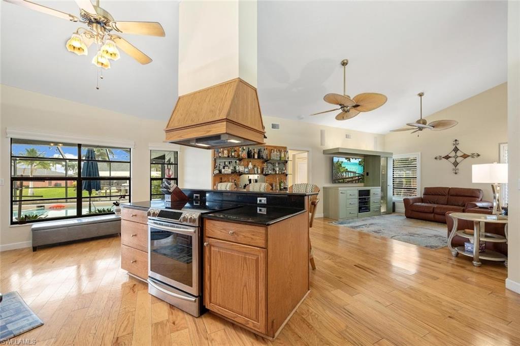 Kitchen featuring ceiling fan, stainless steel range with electric stovetop, high vaulted ceiling, open floor plan, and brown cabinets