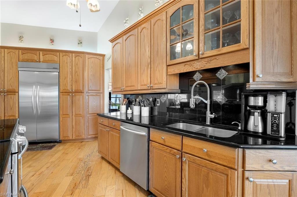 Kitchen with appliances with stainless steel finishes, light wood-style floors, glass insert cabinets, decorative backsplash, and dark stone countertops