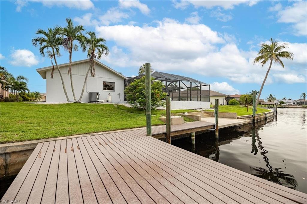 Dock area featuring glass enclosure, a lawn, and a water view