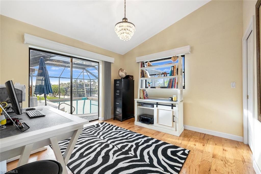Office area featuring light wood-style floors, vaulted ceiling, a sunroom, and a chandelier