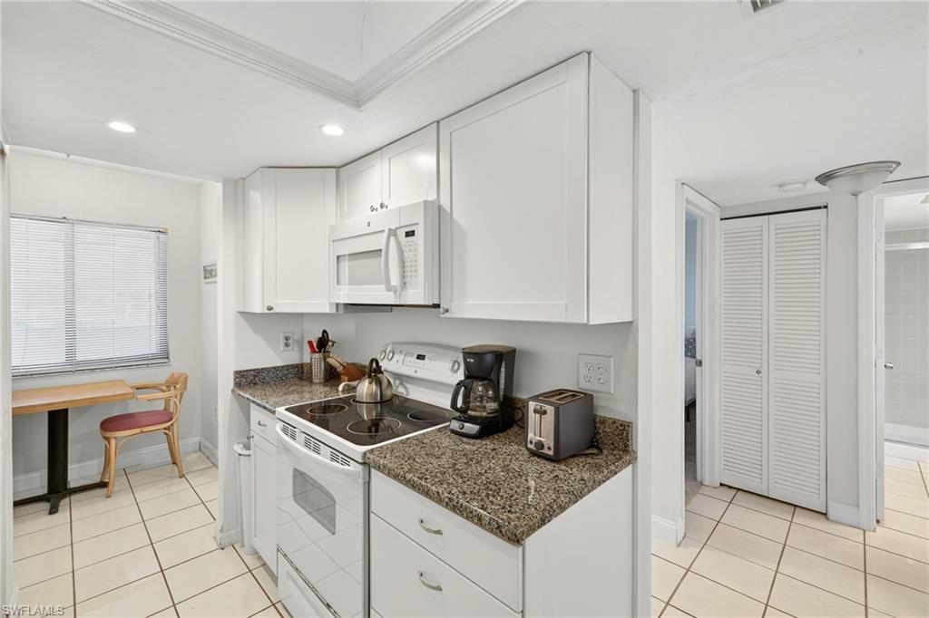 Kitchen with white appliances, light tile patterned flooring, white cabinetry, ornamental molding, and recessed lighting