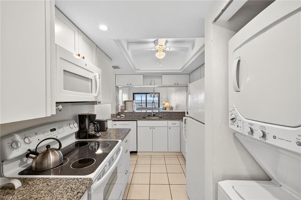Kitchen featuring white appliances, white cabinetry, light tile patterned floors, a raised ceiling, and ceiling fan