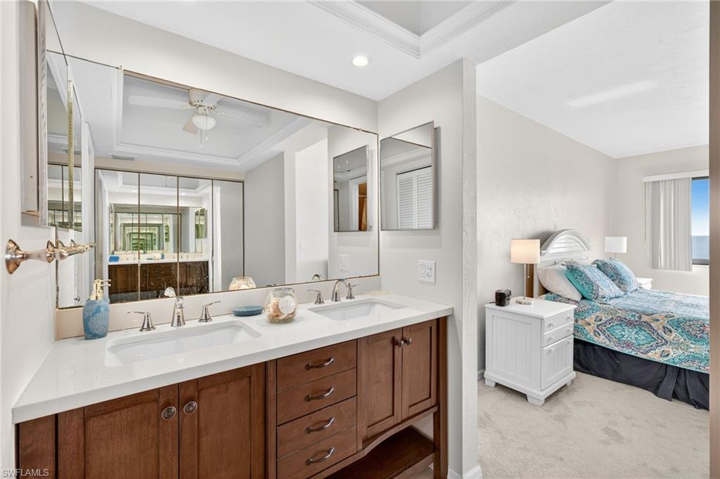 Bathroom with a tray ceiling, double vanity, recessed lighting, ornamental molding, and ensuite bath
