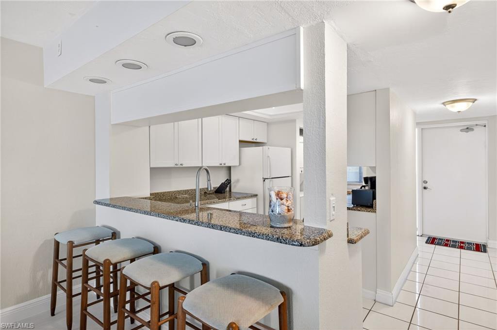 Kitchen featuring white cabinetry, light tile patterned floors, freestanding refrigerator, a kitchen breakfast bar, and dark stone counters