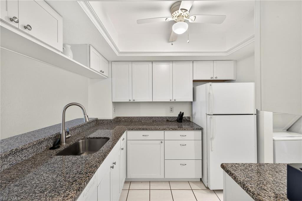 Kitchen with freestanding refrigerator, white cabinets, and light tile patterned flooring