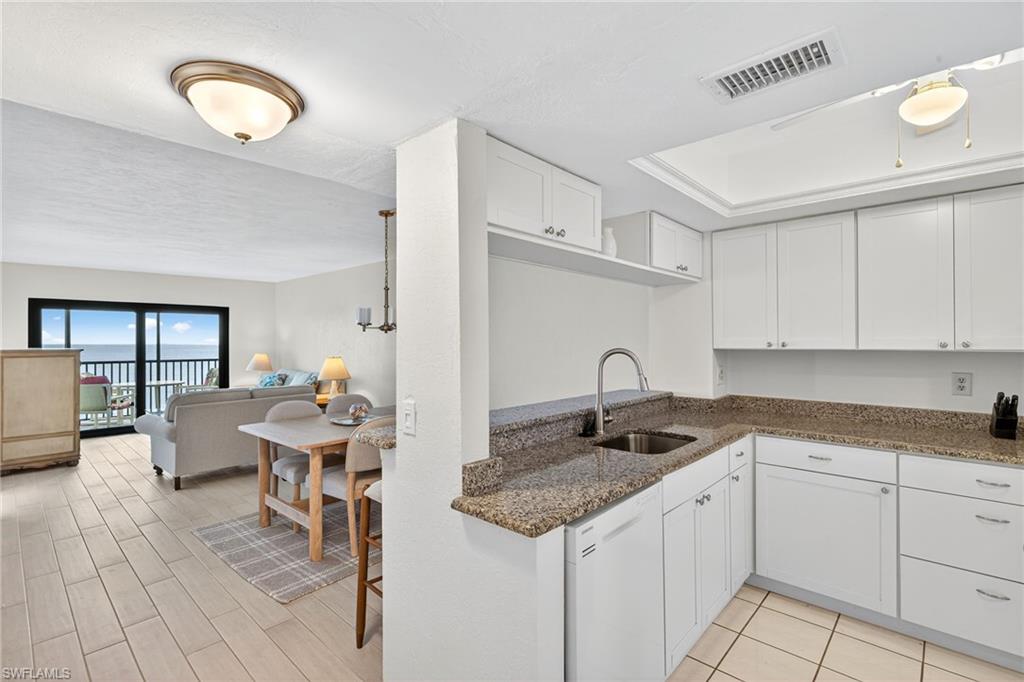 Kitchen featuring dark stone countertops, white cabinetry, white dishwasher, and open floor plan