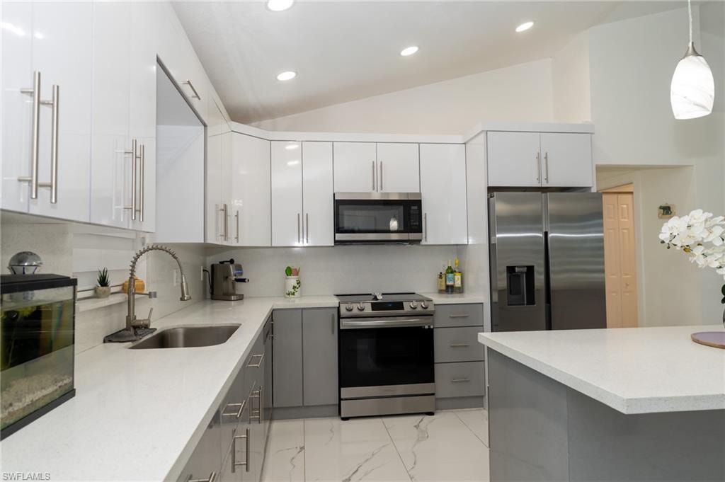 Kitchen with decorative light fixtures, lofted ceiling, stainless steel appliances, gray cabinets, and tasteful backsplash