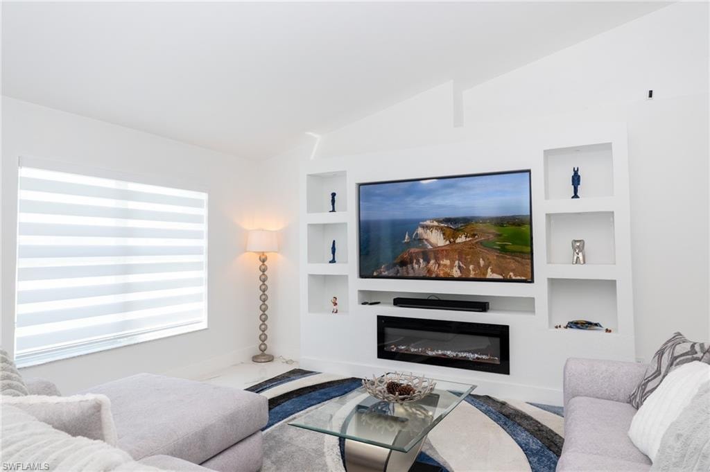 Living room with a glass covered fireplace, vaulted ceiling, and built in features