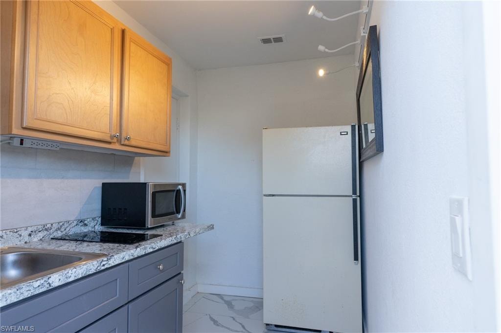 Kitchen with freestanding refrigerator, tasteful backsplash, light marble finish floors, stainless steel microwave, and light stone countertops