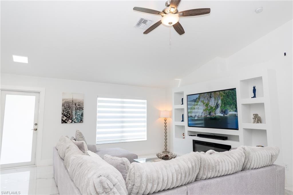 Living room featuring lofted ceiling, a ceiling fan, built in features, and marble look tile flooring