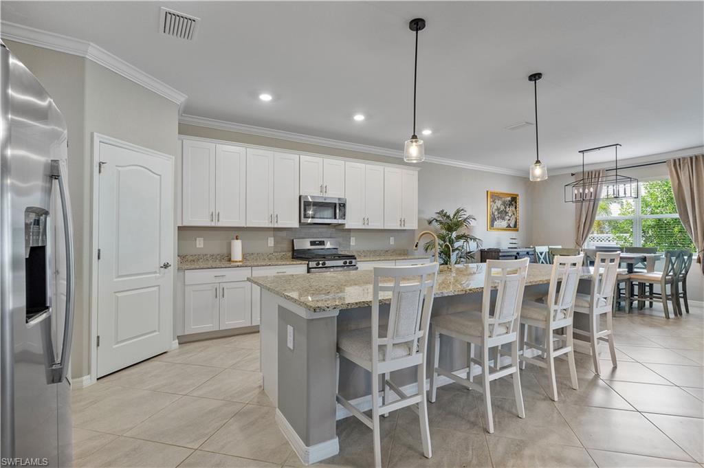 Kitchen featuring a kitchen island with sink, white cabinetry, hanging light fixtures, stainless steel appliances, and light tile patterned floors