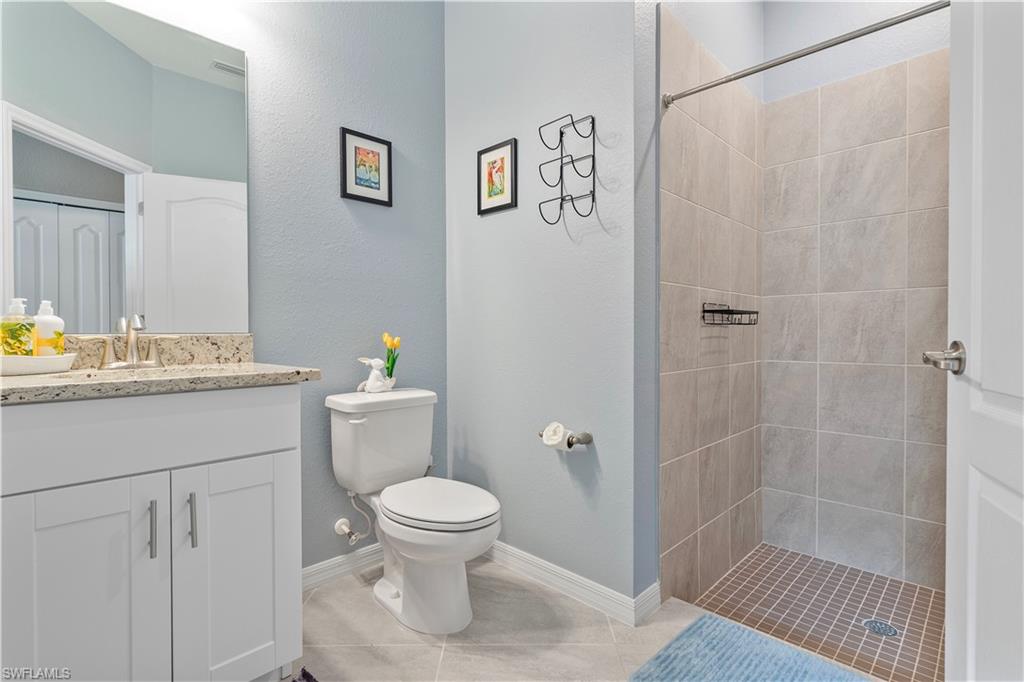 Bathroom with tile patterned flooring, tiled shower, vanity, and toilet