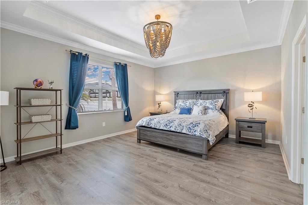 Bedroom with a notable chandelier, a tray ceiling, hardwood / wood-style flooring, and crown molding