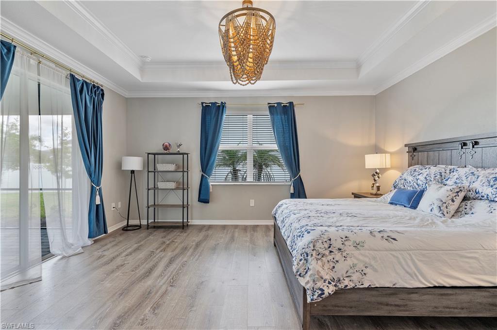 Bedroom featuring wood-type flooring, an inviting chandelier, a raised ceiling, and crown molding