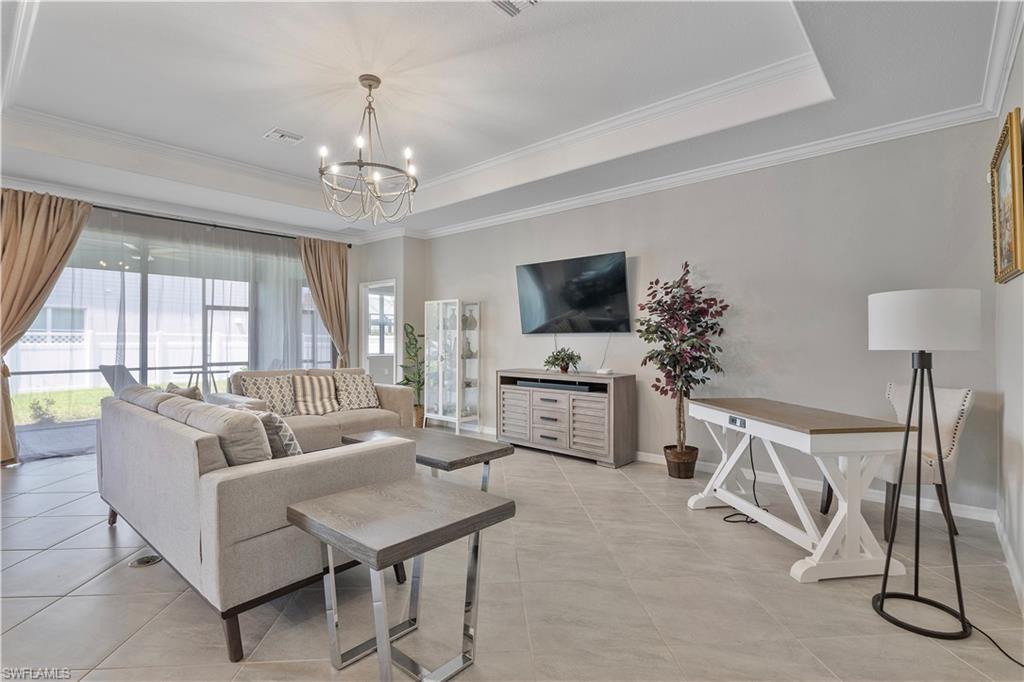 Tiled living room featuring ornamental molding, a raised ceiling, and a chandelier