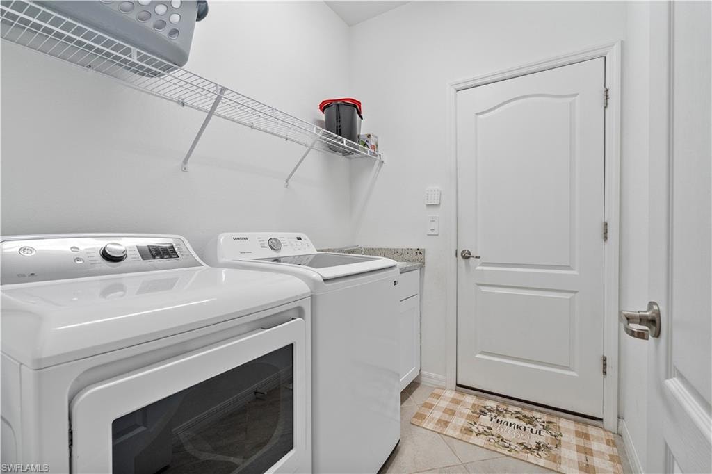 Laundry room featuring cabinets, light tile patterned floors, and washing machine and dryer