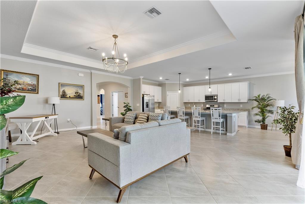 Tiled living room featuring an inviting chandelier, a tray ceiling, and ornamental molding