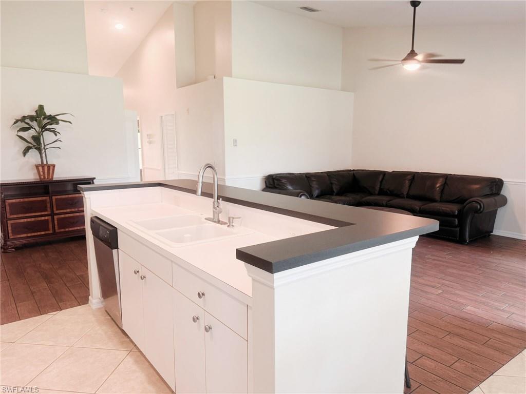 Kitchen with white cabinetry, open floor plan, a center island with sink, dark countertops, and high vaulted ceiling
