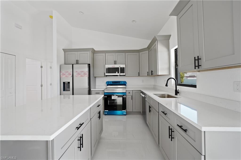 Kitchen featuring gray cabinets, appliances with stainless steel finishes, a kitchen island, lofted ceiling, and light stone countertops