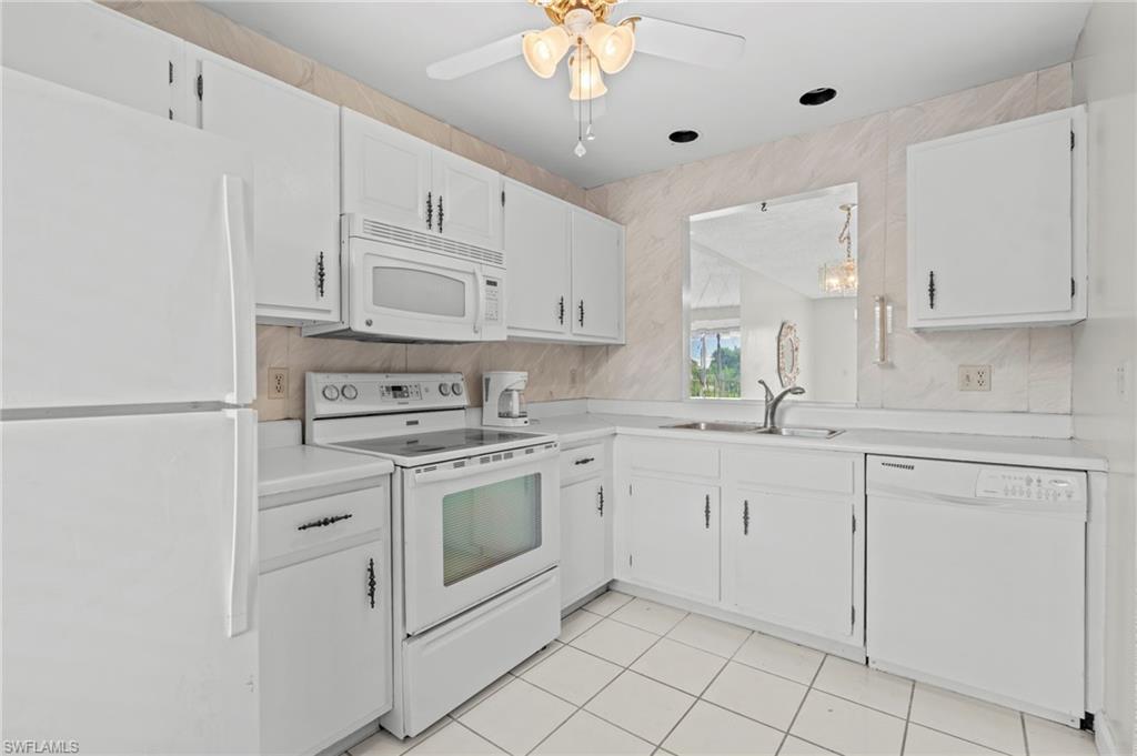 Kitchen with white appliances, light countertops, white cabinets, light tile patterned floors, and a ceiling fan
