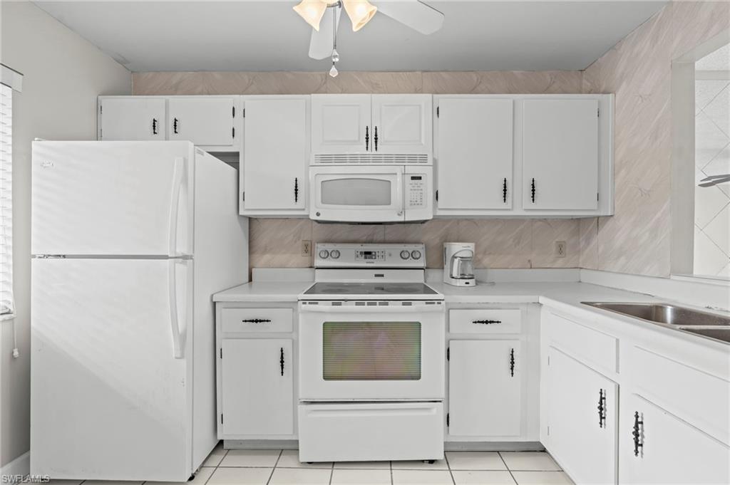 Kitchen featuring white appliances, light countertops, white cabinetry, and light tile patterned floors
