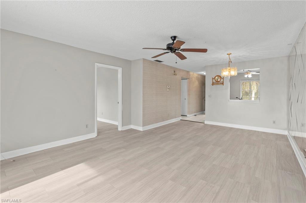 Spare room with light wood-type flooring, a ceiling fan, a chandelier, and a textured ceiling