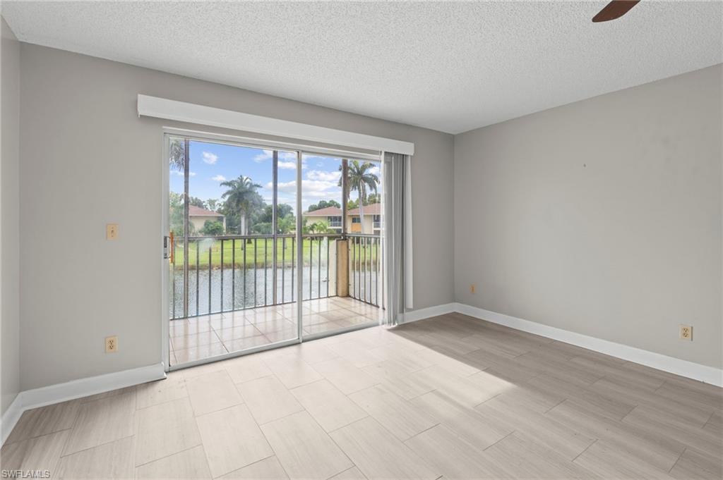 Empty room with a textured ceiling, a water view, ceiling fan, and light wood-style floors