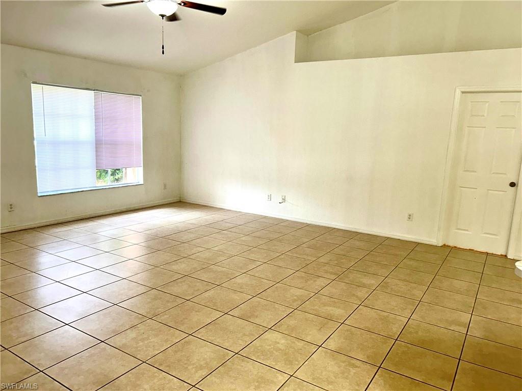 Spare room featuring light tile patterned floors, vaulted ceiling, and a ceiling fan