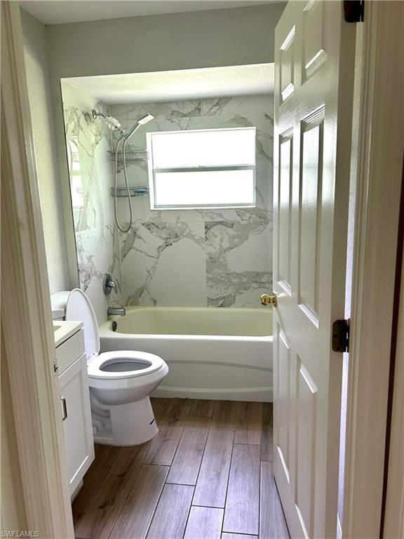 Bathroom featuring a textured wall, bathing tub / shower combination, vanity, and dark wood-type flooring