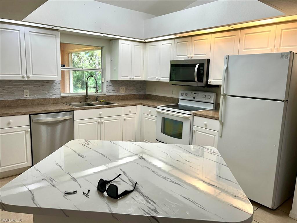 Kitchen featuring appliances with stainless steel finishes, light tile patterned floors, white cabinets, backsplash, and a center island
