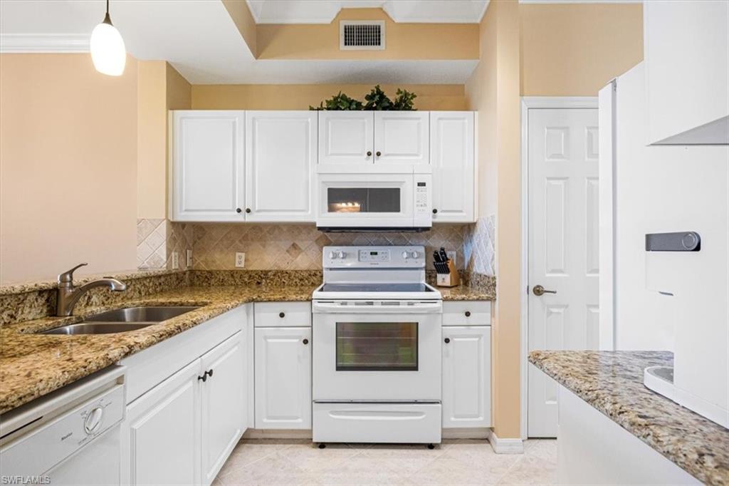 Kitchen with white appliances, white cabinetry, light stone counters, decorative backsplash, and crown molding