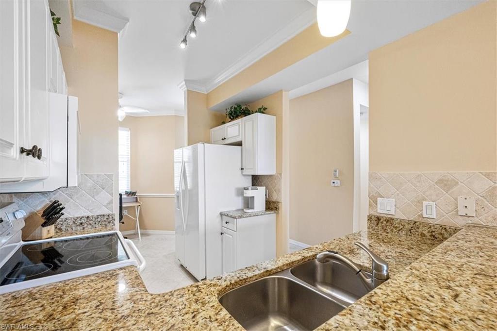 Kitchen with white cabinets, decorative backsplash, ornamental molding, white appliances, and light stone counters